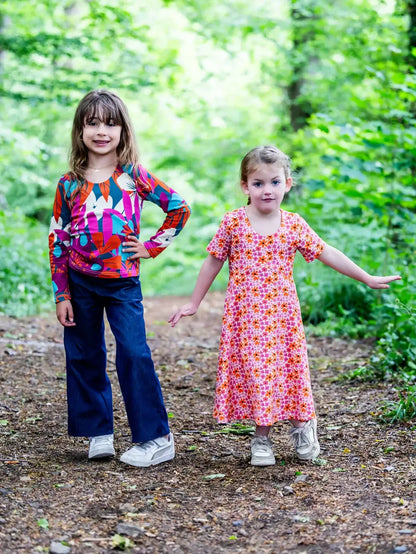 Deux enfants posent dans la forêt portant des vêtements colorés, soulignant la joie des tenues décontractées pour enfants.