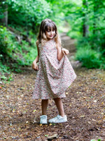 Fillette portant une robe à motifs floraux, debout sur un chemin forestier.