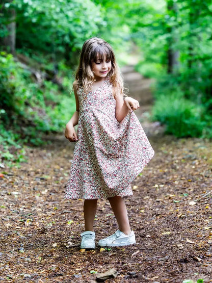 Fillette portant une robe à motifs floraux, debout sur un chemin forestier.