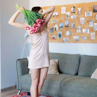 Personne tenant des fleurs portant une nuisette courte, ambiance printemps dans un salon moderne. Nuisette- XXS/L - SPRING BLOOM, patron de couture.