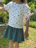 Enfant portant le Patron PDF Jupe Short LILAS & COQUELICOT, short évasé bleu-gris, t-shirt blanc motifs fleuris