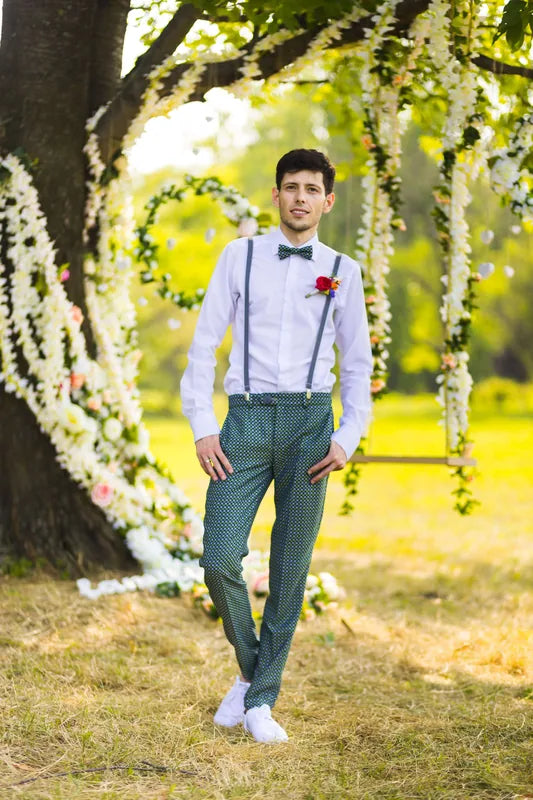 Homme portant un pantalon élégant avec bretelles lors d'un mariage en extérieur, décor floral en arrière-plan.
