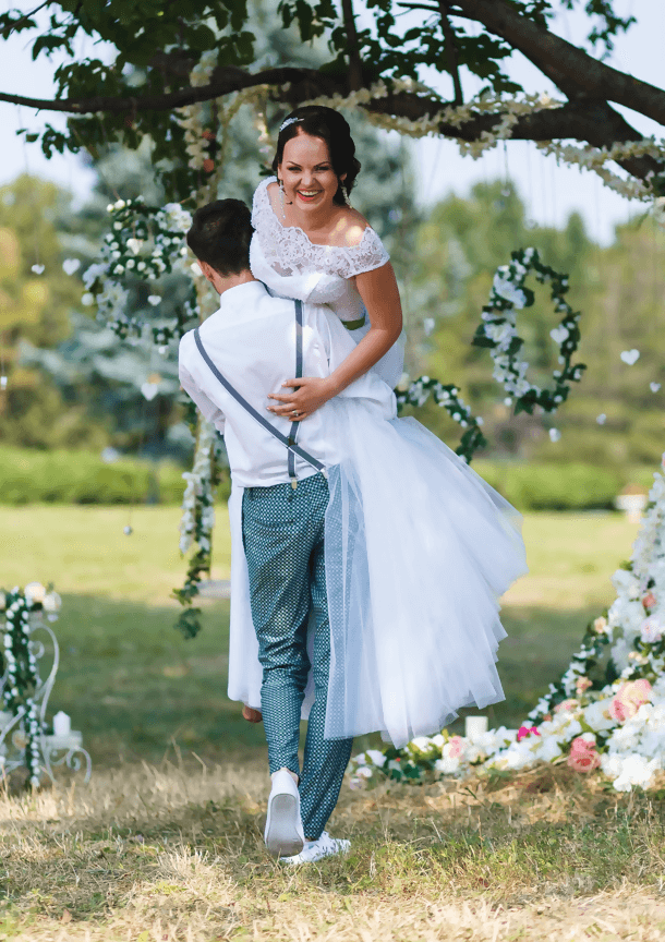 Personne portant une robe blanche, sourire, dans un cadre extérieur fleuri.