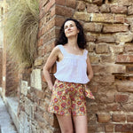 Femme portant un short Orsi avec motif floral, conçu avec le patron de couture pdf à télécharger, contre un mur de briques.