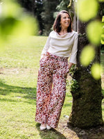 Femme portant le Patron PDF Blouse Bénitier PINA COLADA, manches longues en coton, pantalon fleuri, sous un arbre moussu