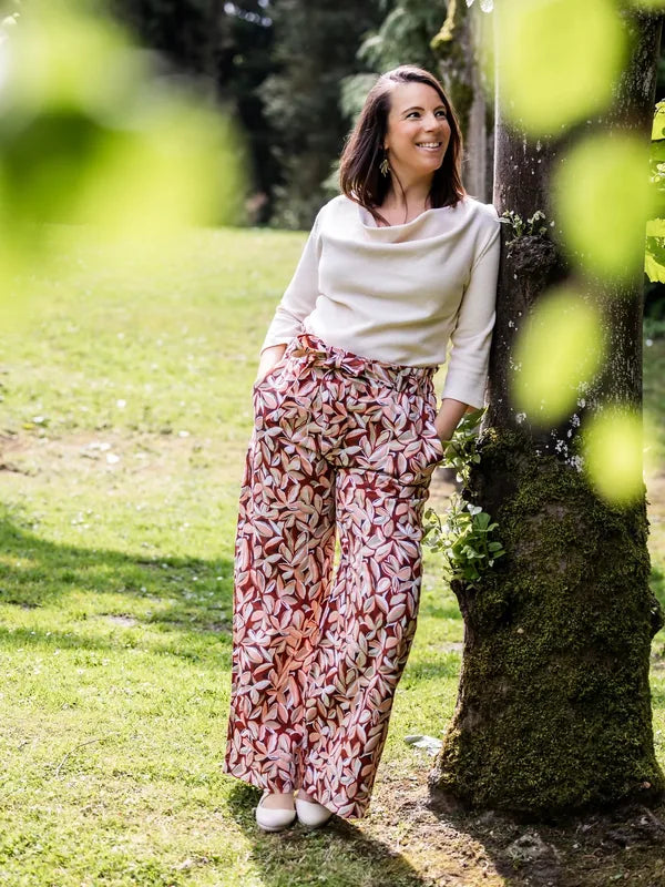 Femme portant le Patron PDF Blouse Bénitier PINA COLADA, manches longues en coton, pantalon fleuri, sous un arbre moussu