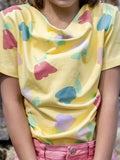 Enfant portant le Patron PDF Blouse Bénitier PINA COLADA en coton jaune, motifs floraux colorés, vue de face