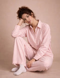 Femme portant le Patron PDF Ensemble Blouse & Pantalon Pyjama ROSIE en coton à rayures roses, assise en coton blanc