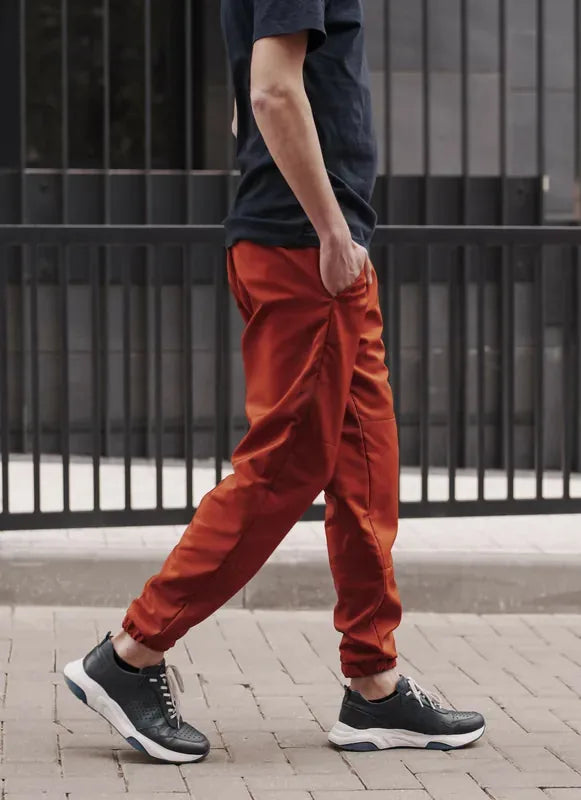 Homme portant le Patron PDF Comfortino en sergé rouge, jogging ajusté, vue de profil en mouvement devant portail gris