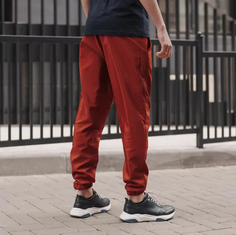Homme portant le Patron PDF Comfortino, jogging rouge bordeaux, vue de dos, devant portail gris