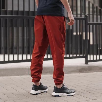 Homme portant le Patron PDF Comfortino, jogging rouge bordeaux, vue de dos, devant portail gris