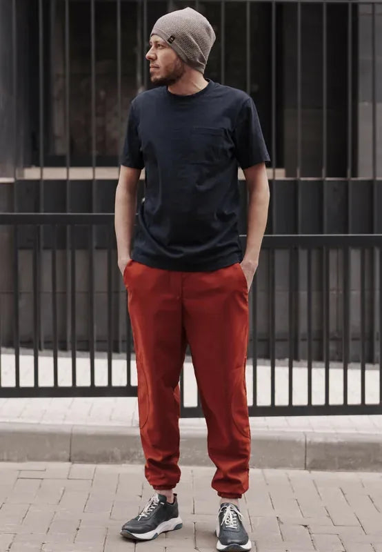 Homme portant le Patron PDF Comfortino, pantalon rouge et t-shirt noir, bonnet gris, devant portail métallique