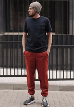 Homme portant le Patron PDF Comfortino, pantalon rouge et t-shirt noir, bonnet gris, devant portail métallique