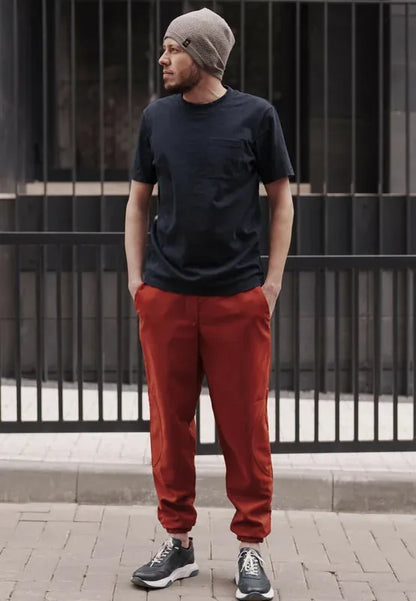 Homme portant le Patron PDF Comfortino, pantalon rouge et t-shirt noir, bonnet gris, devant portail métallique