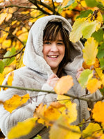 Femme portant un manteau d'automne parmi les feuilles jaunes.