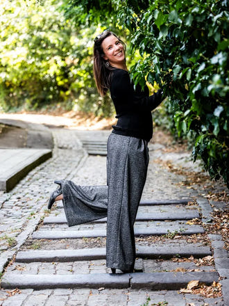 Femme portant le Patron PDF PECAN pantalon à plis en sergé gris, vue de côté dans une allée de verdure