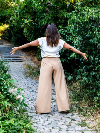 Femme portant le Patron PDF PECAN pantalon à plis, vue de dos dans un jardin avec allée pavée
