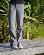 Femme portant le Patron PDF Pantalon Q du 32 au 60, vue de profil en coton gris, sur une terrasse en bois