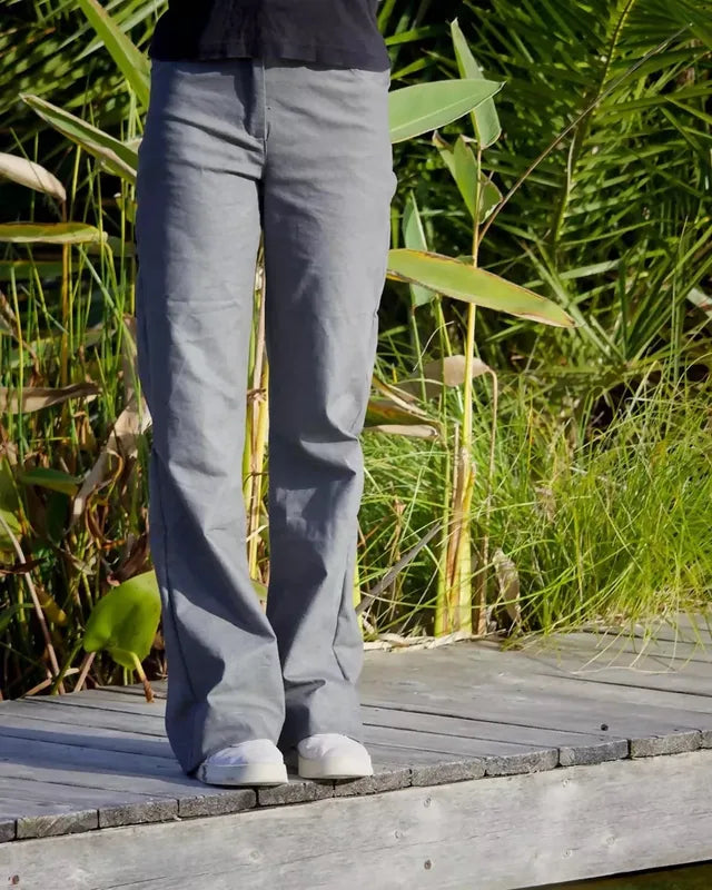 Femme portant le Patron PDF Pantalon Q du 32 au 60, vue de profil en coton gris, sur une terrasse en bois