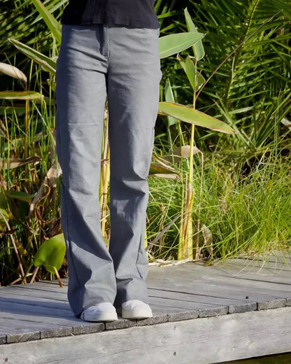 Femme portant le Patron PDF Pantalon Q du 32 au 60, vue de profil en coton gris, sur une terrasse en bois