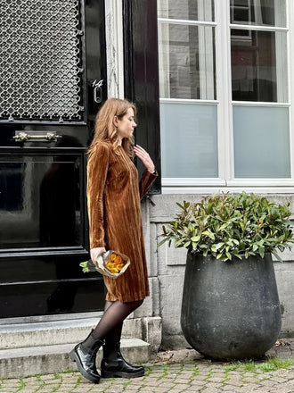 Femme portant le Patron PDF Robe Zoya en velours côtelé marron, devant une porte noire