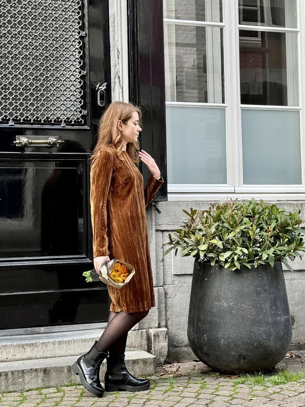 Femme portant le Patron PDF Robe Zoya en velours côtelé marron, devant une porte noire