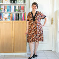 Femme portant le Patron PDF Robe courte Pomme Golden, manches courtes à fleurs orangées et noires, devant une bibliothèque