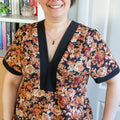 Femme portant le Patron PDF Robe courte Pomme Golden, manches courtes, col en V avec bande noire contrastante, imprimé roses
