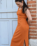 Femme portant le Patron PDF Robe Cotelle du 32 au 52, robe longue orange avec fente, appuyée contre brique
