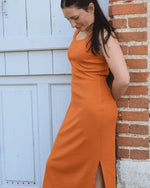 Femme portant le Patron PDF Robe Cotelle du 32 au 52, robe longue orange avec fente, appuyée contre brique
