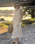 Femme portant le Patron PDF Robe Aliz du 32 au 52, robe longue boutonnée en lin blanc, au bord d'une rivière