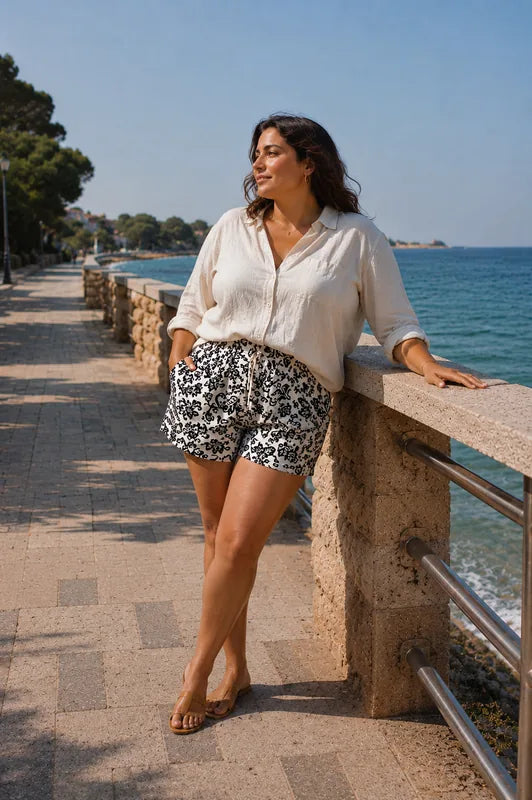 Femme portant le Patron PDF Short Figuette du 34 au 54, short blanc à motifs noirs, en bord de mer méditerranéenne