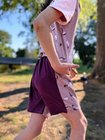 Enfant portant le Patron PDF Short TWIST, short bicolore rose et prune, vue de profil en extérieur