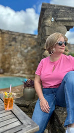 Femme portant le Patron PDF T-Shirt Femme Zestia en coton rose, vue de face près d'une piscine, ruines en arrière-plan