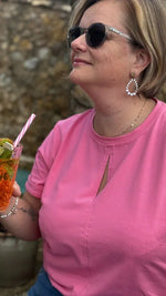 Femme portant le Patron PDF T-Shirt Femme Zestia du 32 au 52 en rose, vue de côté contre un mur en pierre
