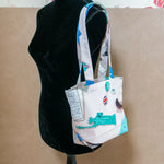 Tote bag blanc porté sur mannequin, motifs turquoise et Union Jack, anses longues, vue de profil