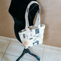 Petit Tote Bag avec fond en coton écru, motifs couture bleus et oranges, porté à l'épaule