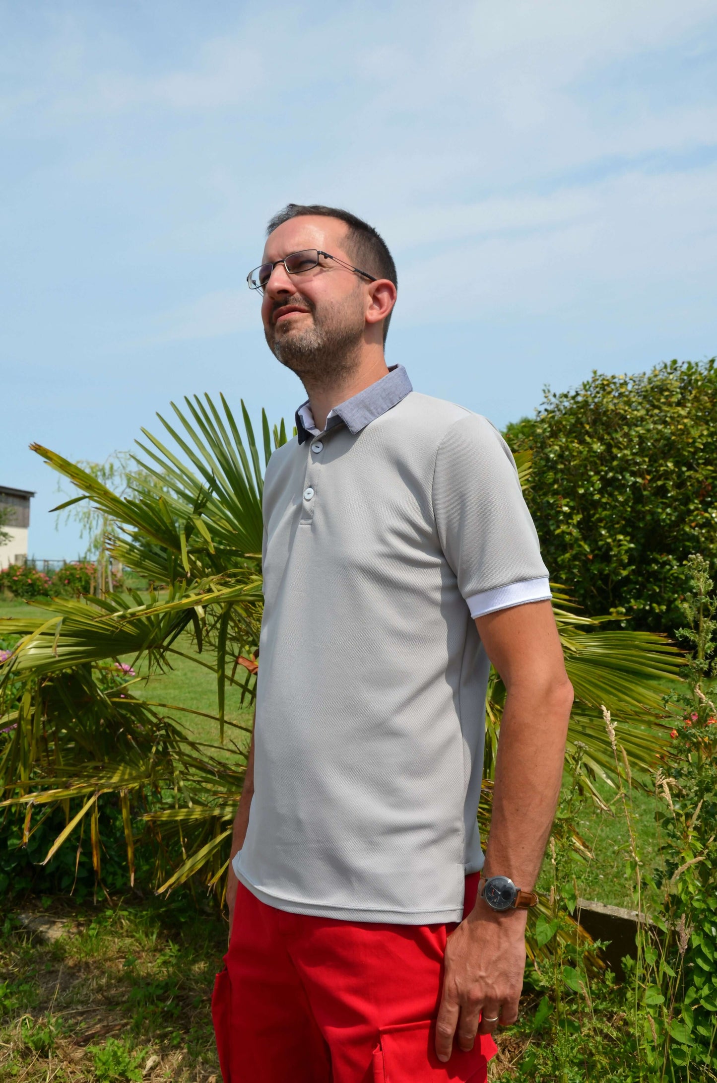 Homme portant un Polo LOPO gris avec patron de couture pdf à télécharger, manches courtes et col officier, posé dans un jardin.