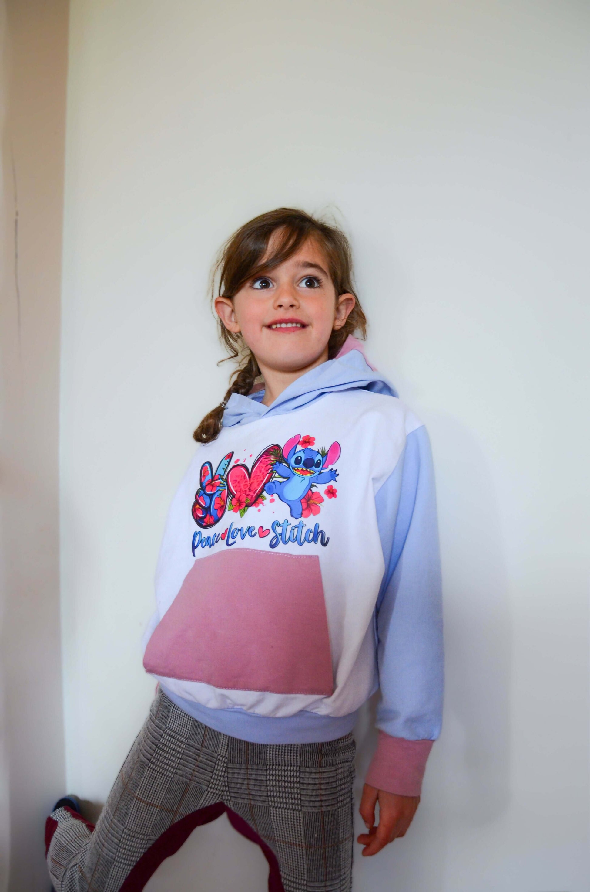 Jeune fille portant un sweat à capuche coloré, décoré de motifs vibrants, se tenant contre un mur blanc.
