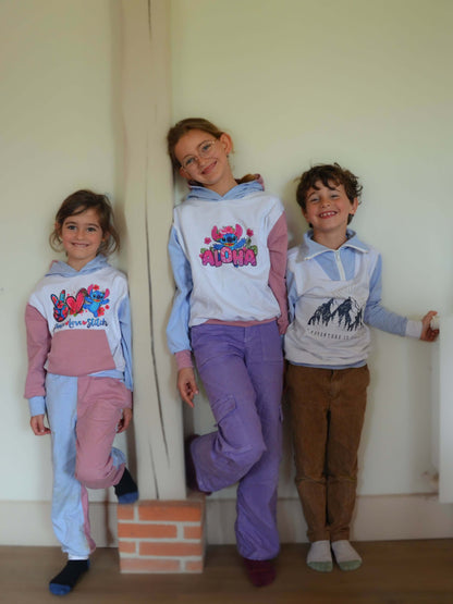 Trois enfants souriants portant des pulls colorés dans une maison.