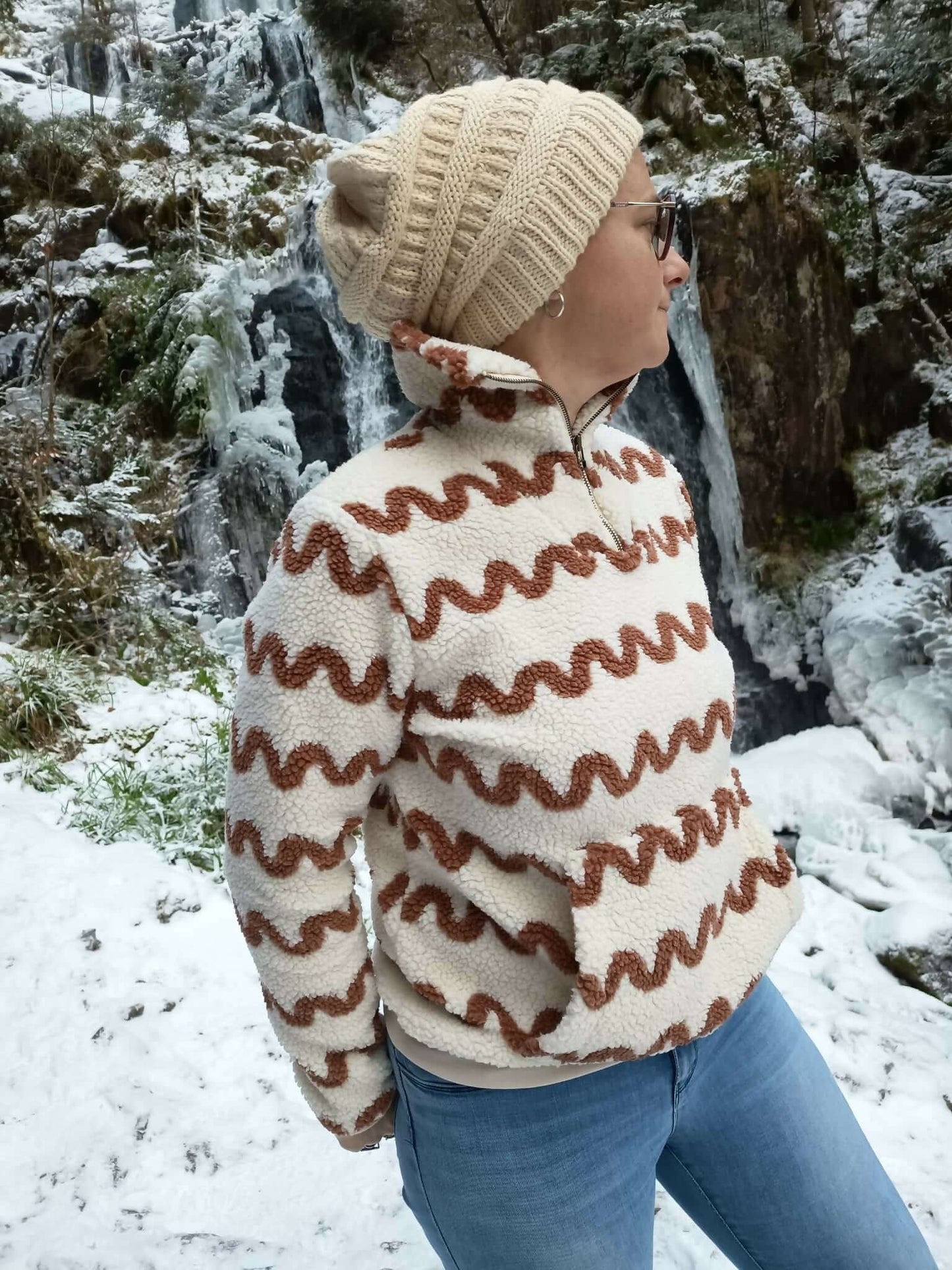 Personne portant un pull camionneur élégant devant une cascade enneigée, idéal pour patron de couture pdf à télécharger.