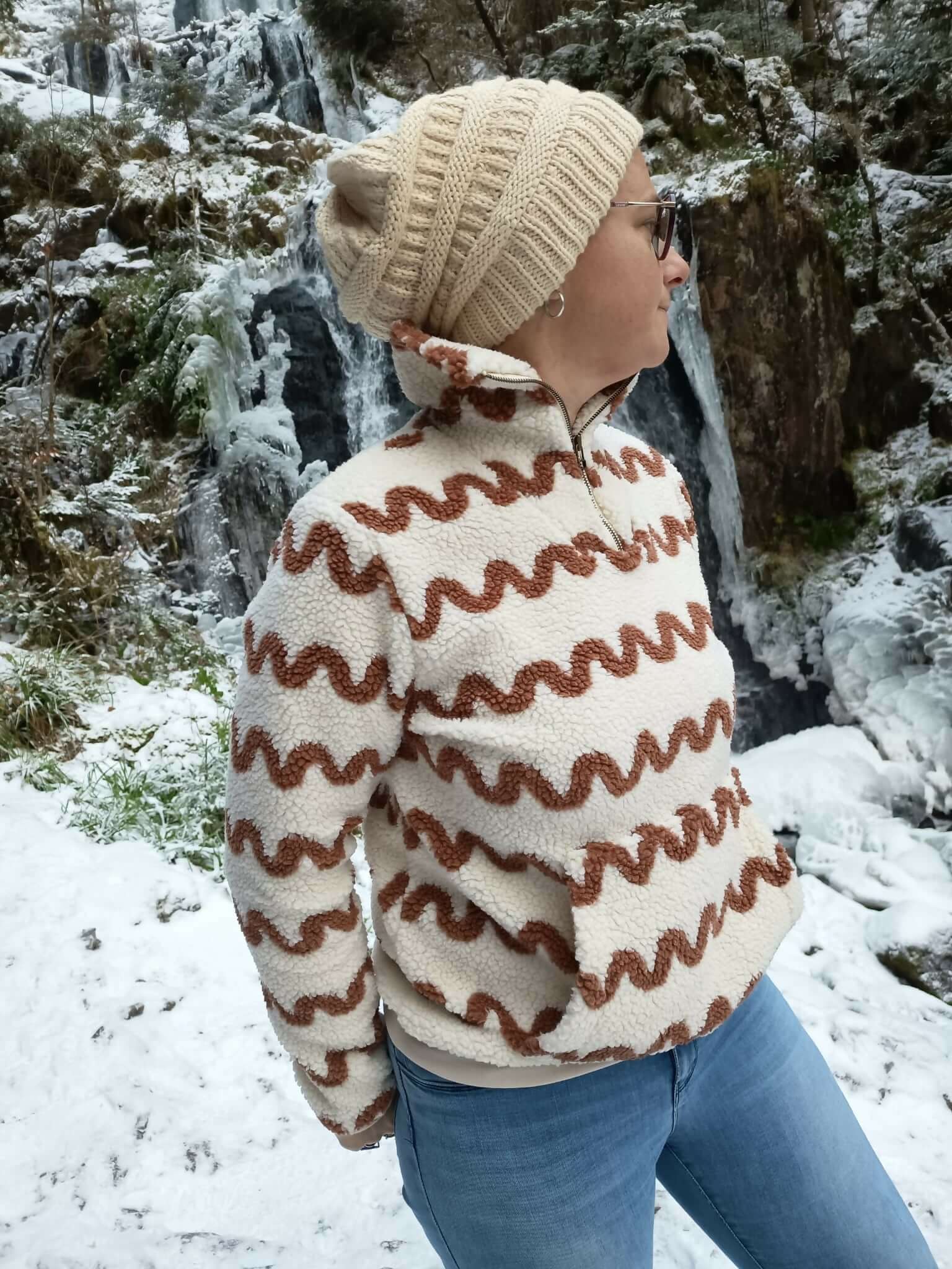 Personne portant un pull camionneur élégant devant une cascade enneigée, idéal pour patron de couture pdf à télécharger.