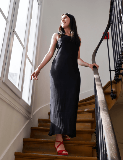 Femme portant la Robe Aury noire, patron de couture pdf à télécharger, en montant un escalier élégant avec des sandales rouges.