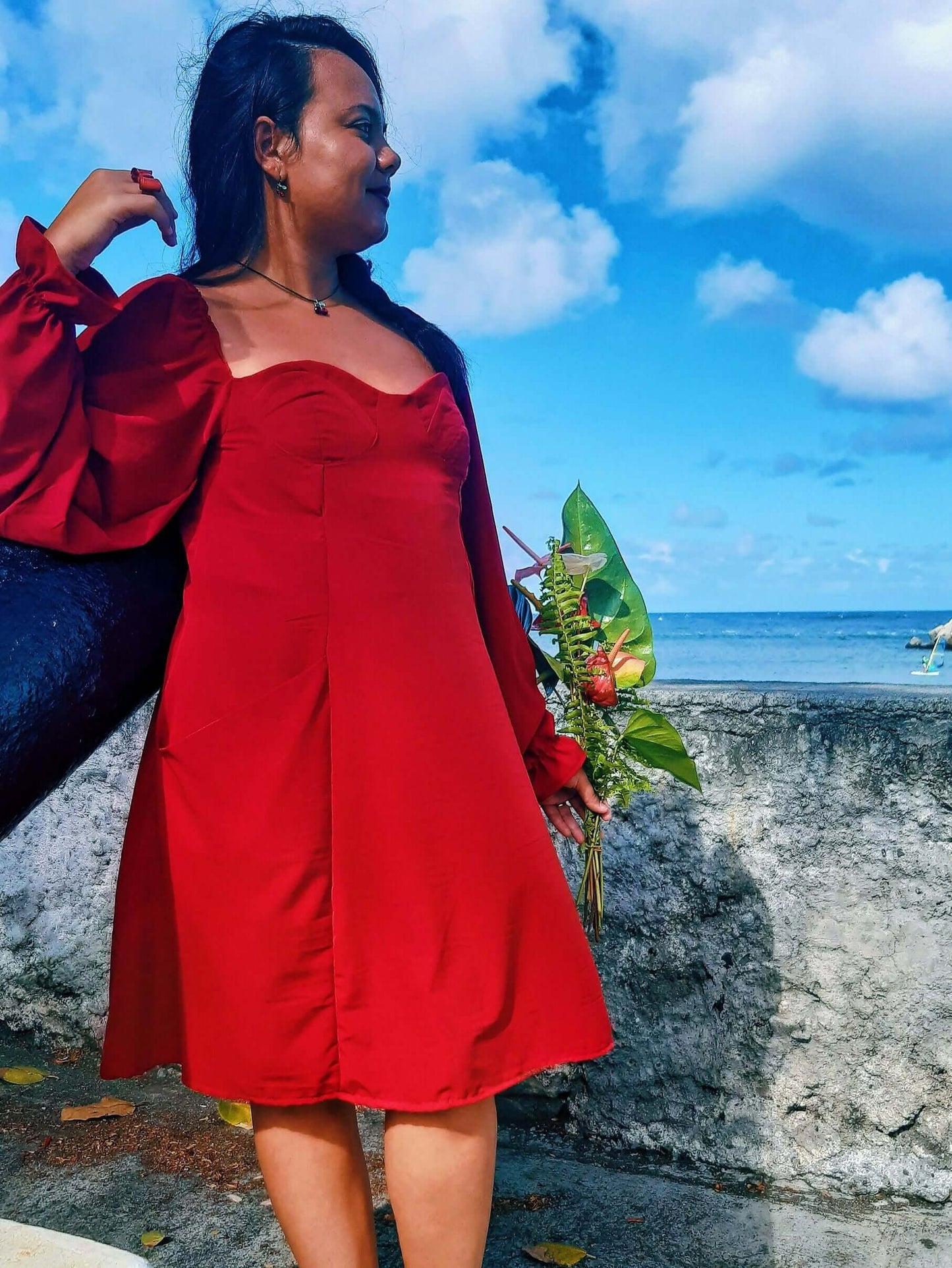 Femme portant une Robe Cassiopée - T36 à 50 rouge avec manches bouffantes, près de la mer, patron de couture pdf à télécharger.