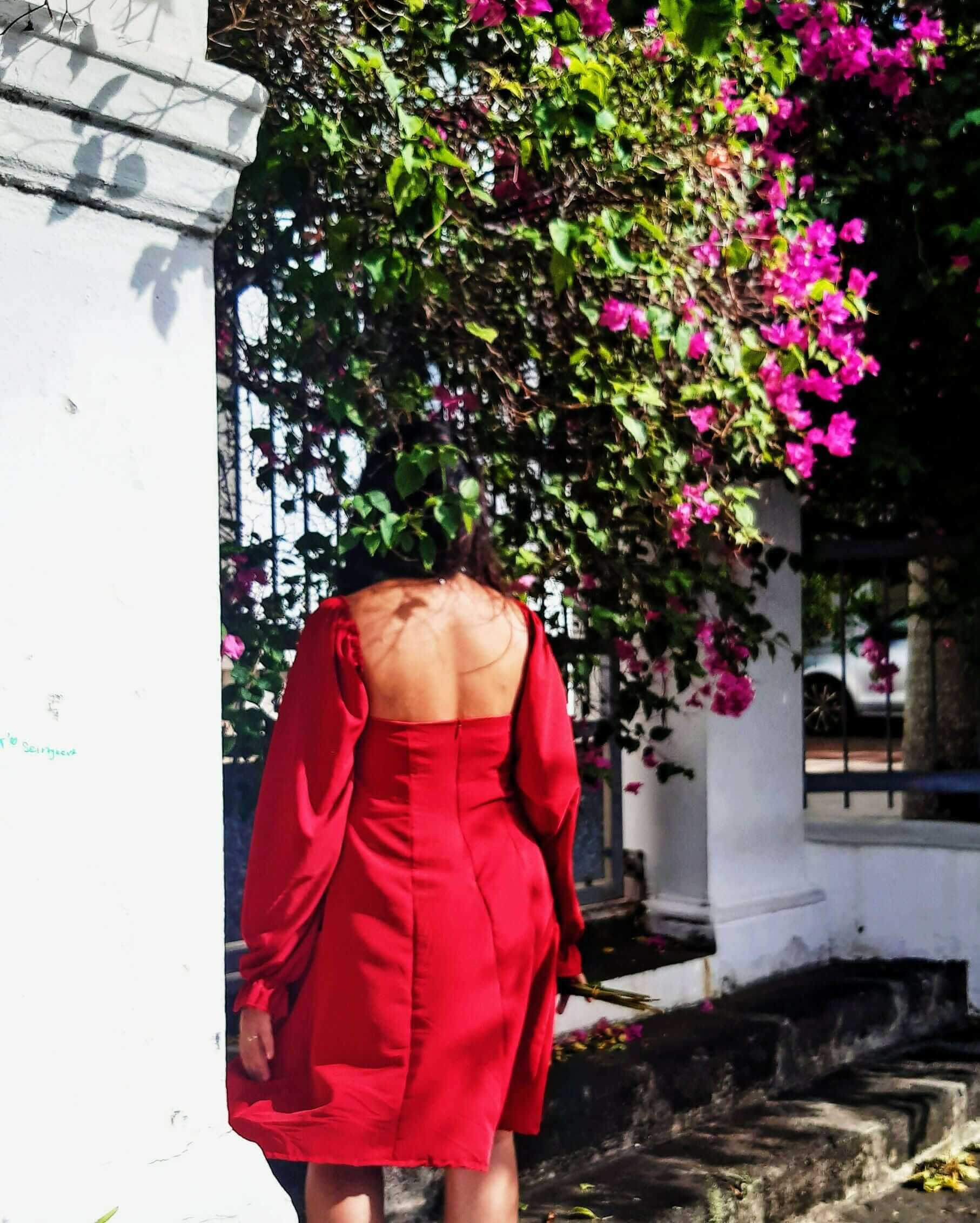 Femme portant la Robe Cassiopée - T36 à 50 avec un dos nu et manches bouffantes, se tenant près de fleurs roses, patron de couture pdf à télécharger