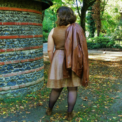 Femme portant la Robe Cilaos - 32 au 56, un patron de couture pdf à télécharger, dans un parc, avec une veste en cuir sur l'épaule.