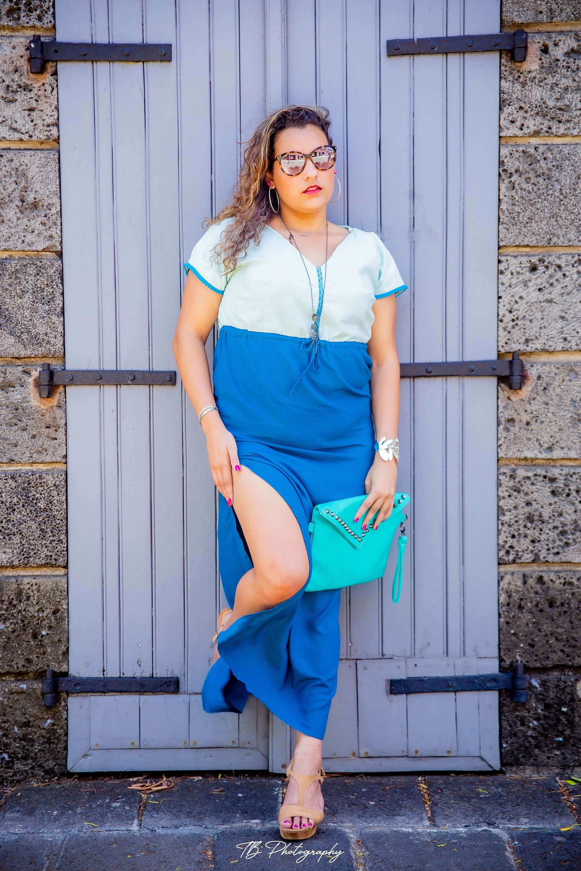 Femme posant avec une robe longue bleue et blanche, tenue d'été mode, devant une porte en bois.