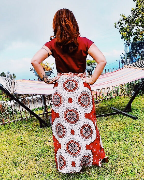 Femme portant une jupe longue imprimée rouge avec motifs circulaires devant un hamac dans le jardin.