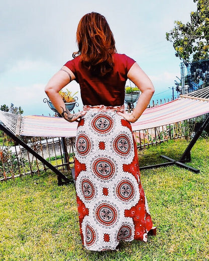 Femme portant une jupe longue imprimée rouge avec motifs circulaires devant un hamac dans le jardin.