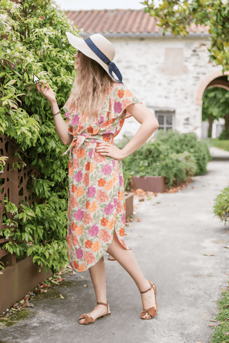 Femme portant une robe FLORISSE colorée avec un chapeau, posant dans un jardin, idéale pour un patron de couture.